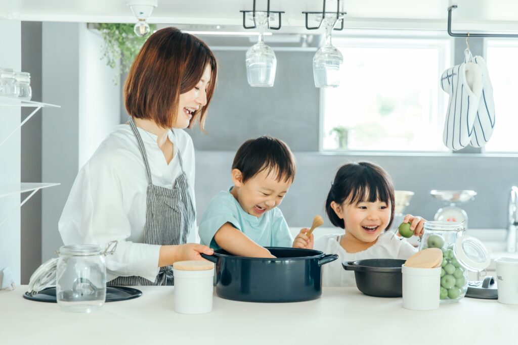キッチンで母親と幼い子供２人が料理をしている。みんな笑顔の様子。