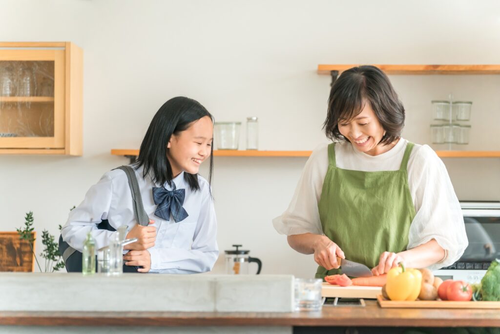 母と娘がキッチンで楽しそうに笑顔でいる。母は料理をしている。